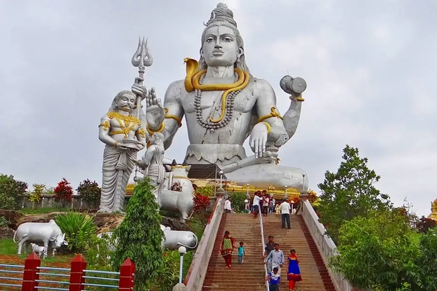Massive white statue of Lord Shiva seated with a trident and a snake, atop steps with visitors climbing