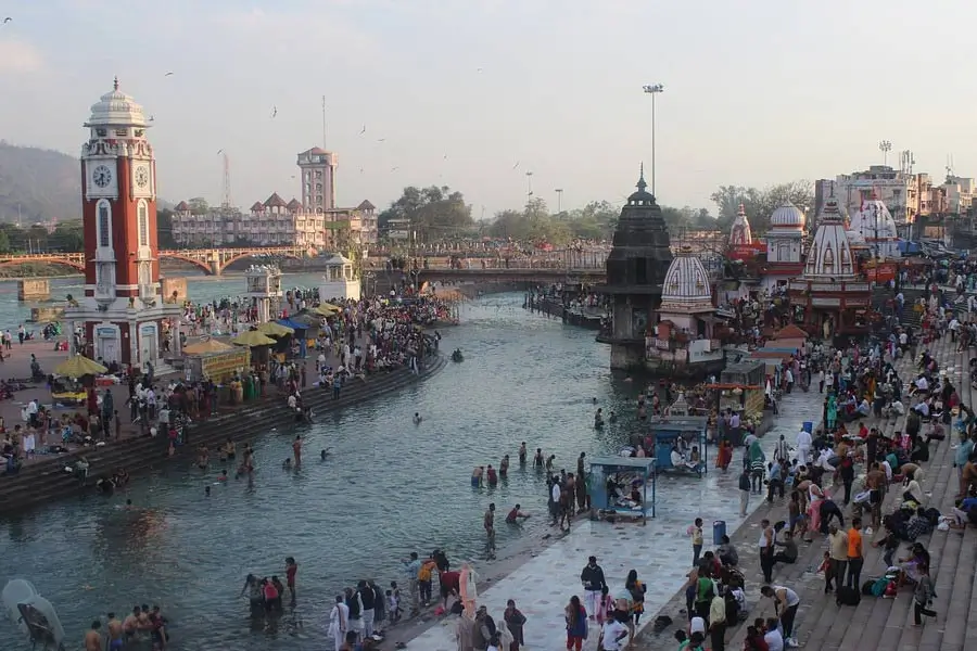 Crowded riverside ghats with temples and a tall clock tower along a wide river.