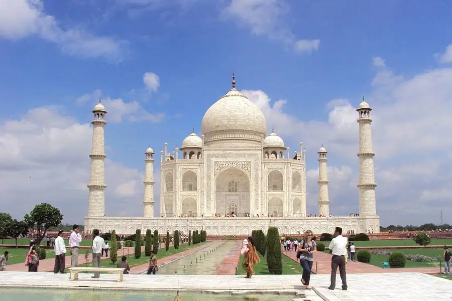 Taj Mahal with blue sky, white marble mausoleum, and surrounding gardens with visitors in foreground